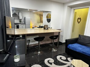 Eine moderne Küche mit einer zentralen Kochinsel, zwei Barhocker, einem schwarzen Sofa und einem kleinen Couchtisch.