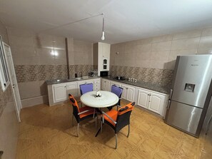 Eine Küche mit einem runden Tisch, Stühlen, Schränken, einem Kühlschrank und einer Pendelleuchte.