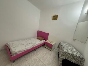 Ein kleines Schlafzimmer mit einem Einzelbett, einem Nachttisch, einem kleinen Tisch und einem an der Wand befestigten Spiegel.