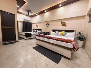 Habitación de hotel con una cama grande, una cama más pequeña, un escritorio, una silla, una planta en maceta y una puerta.
