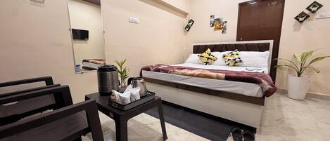 Habitación de hotel con cama, mesita de noche con hervidor, planta pequeña y espejo en la pared.