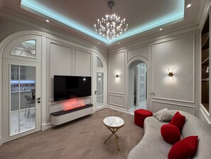 A modern living room with a flat-screen TV, a fireplace, a red sofa, and a chandelier. - Stylish stay in a heart of Yerevan between Republic Square and Opera (Yerevan)
