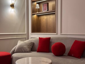 A modern living room with a grey sofa, red cushions, a round coffee table, and a wooden shelf with a lamp and a framed item. - Stylish stay in a heart of Yerevan between Republic Square and Opera (Yerevan)