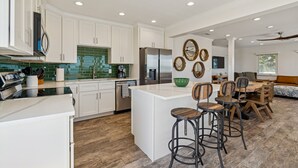 Una cocina moderna con armarios blancos, un refrigerador de acero inoxidable y una zona de comedor con sillas y una mesa de madera.