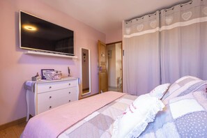 Ein Schlafzimmer mit Bett, Kommode, Spiegel und Fernseher an der Wand.
