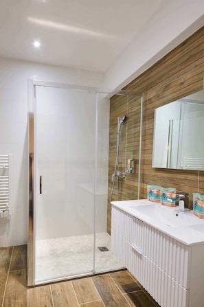 A modern bathroom with a glass shower enclosure, a white vanity, and a wooden wall panel. - Cozy flat, Halles view, AC · MyLocTravel (Béziers)