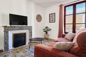A living room with a fireplace, a television, a sofa, a small table, and a potted plant. - Cozy flat, Halles view, AC · MyLocTravel (Béziers)