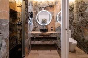 Ein Badezimmer mit Marmorwaschtisch, einem runden Spiegel mit Beleuchtung, einem schwarzen Waschbecken und einer Toilette.