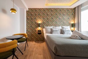 A hotel room with a bed, two wall-mounted lights, a small table with a chair, and a patterned wallpaper. - Sol Atelier | Apartments by Monaro* * * * * (Madrid)