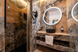 A bathroom with a marble wall, a sink with a black basin, a towel rack, and a hairdryer on the wall. - Sol Atelier | Apartments by Monaro* * * * * (Madrid)