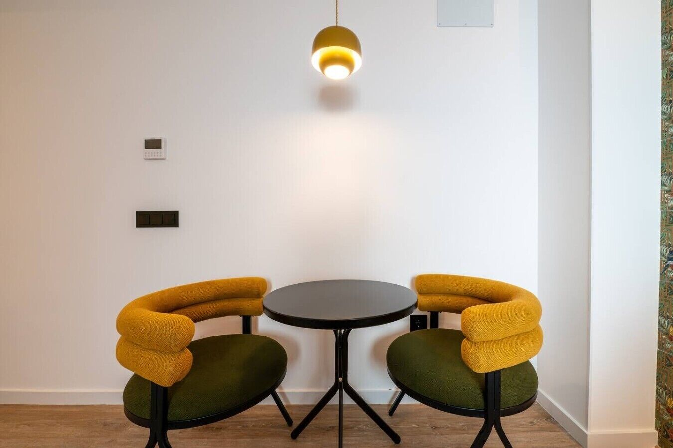 Una habitación con una mesa redonda y dos sillas con tapicería amarilla, una lámpara colgante y un termostato en la pared.