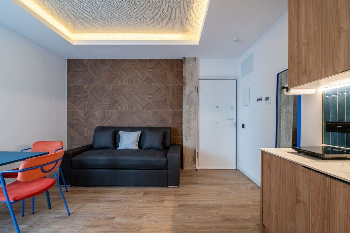 Een moderne kamer met een zithoek, een eettafel met stoelen, een kitchenette en een kamer met een patroon op de muur.