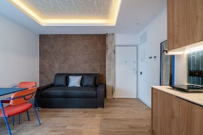 A modern room with a sofa, a dining table with chairs, a kitchenette, and a patterned wall. - Sol Atelier | Apartments by Monaro* * * * * (Madrid)