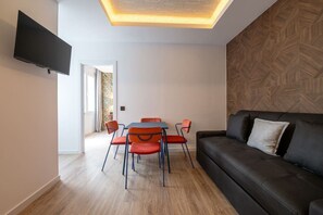 A modern living room with a flat-screen TV, a black leather sofa, and a dining area with red chairs. - Sol Atelier | Apartments by Monaro* * * * * (Madrid)