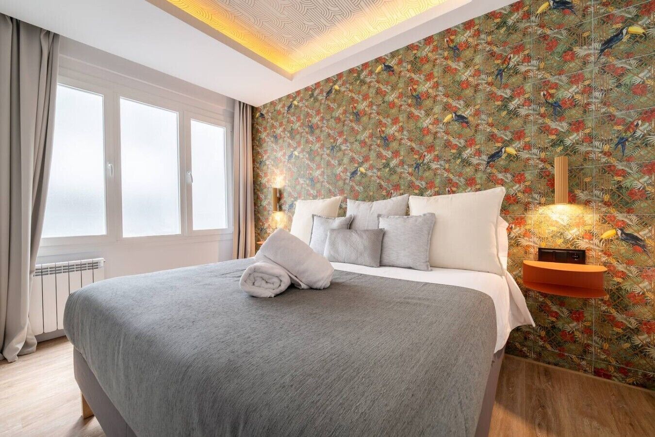 Ein Hotelzimmer mit einem großen Bett, einem Fenster mit Vorhängen, einer Wand mit Muster und einem Nachttisch mit einer Lampe.