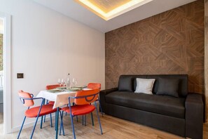 Ein modernes Interieur mit einem für zwei Personen gedeckten Esstisch, einer schwarzen Couch mit Kissen und einer Wand mit Muster.