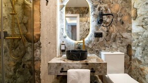 Et badeværelse med en marmorvæg, et spejl med gylden ramme, en sort vask, et hvidt toilet og en bruseniche med et gyldent brusehoved.