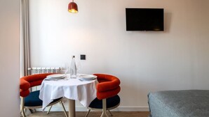 A hotel room with a dining table set for two, a flat-screen TV mounted on the wall, and a bed with a grey cover. - Sol Atelier | Apartments by Monaro* * * * * (Madrid)