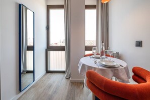 A dining area with a round table set for two, a mirror on the wall, and a view through the window. - Sol Atelier | Apartments by Monaro* * * * * (Madrid)
