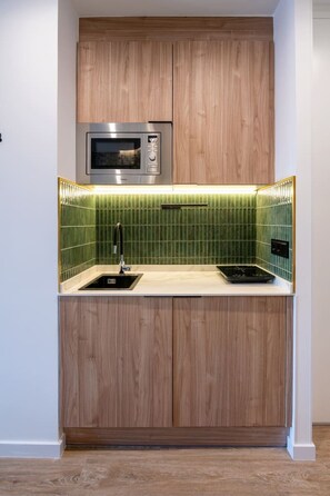 A compact kitchen with a built-in microwave, a sink, and a green-tiled backsplash. - Sol Atelier | Apartments by Monaro* * * * * (Madrid)