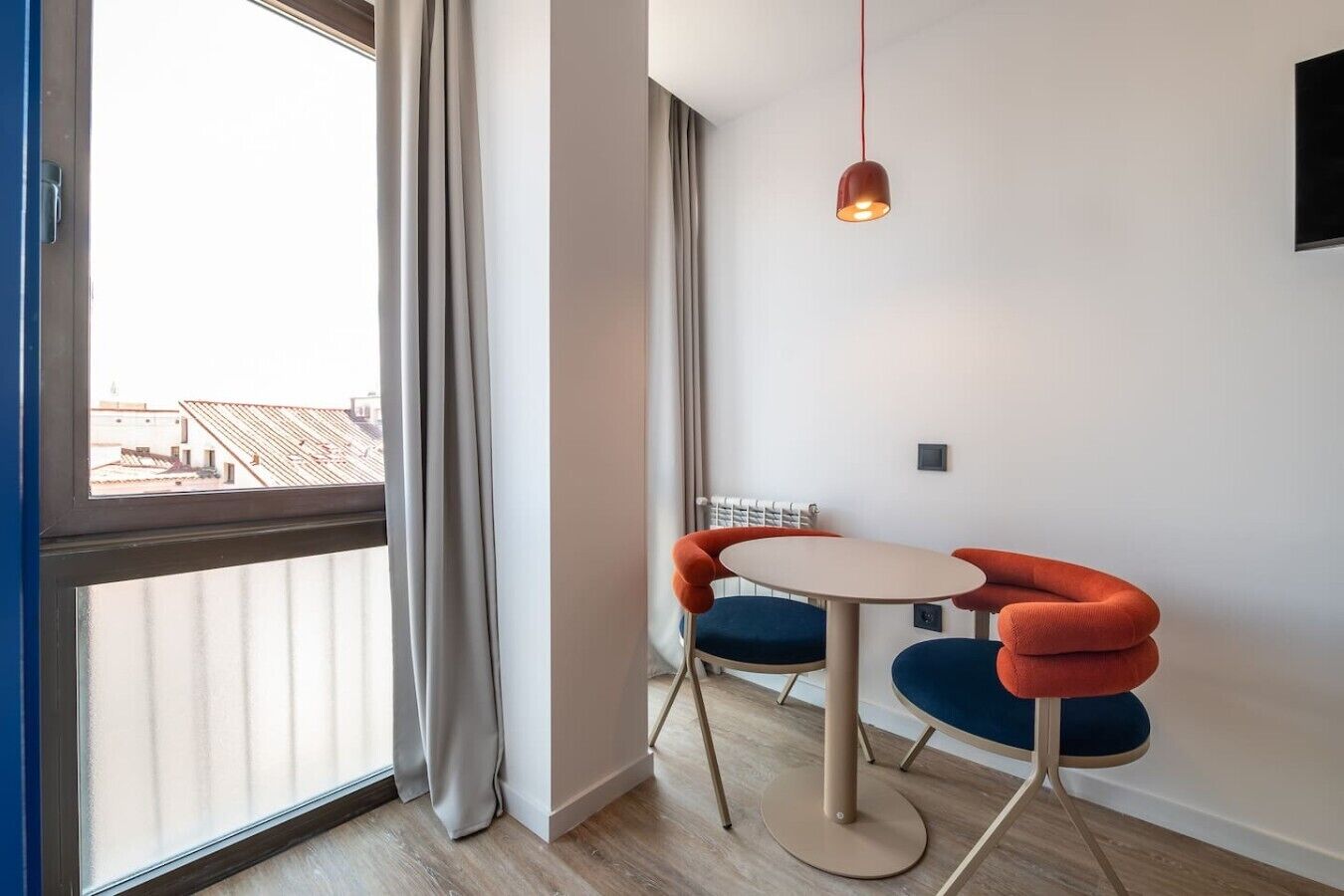 Ein modernes Zimmer mit einem großen Fenster, einem runden Tisch mit zwei Stühlen und einer Hängelampe.