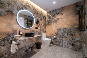 Ein modernes Badezimmer mit Marmorwand, einem runden Spiegel, einem Waschbecken und einer Toilette.