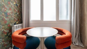 A room with a round table, orange armchairs, a radiator, and a window with curtains. - Sol Atelier | Apartments by Monaro* * * * * (Madrid)