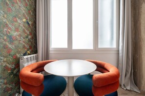 A room with a round table, orange armchairs, a radiator, and a window with curtains. - Sol Atelier | Apartments by Monaro* * * * * (Madrid)