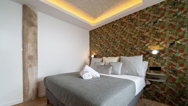 A modern bedroom with a large bed, a wooden accent wall, and a floral-patterned wallpaper. - Sol Atelier | Apartments by Monaro* * * * * (Madrid)
