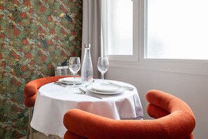 Een eettafel gedekt met een witte tafelkleed, borden, bestek en twee glazen, met een fles en een decoratief object op tafel.