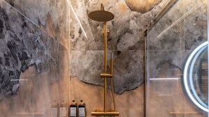 A modern bathroom with a marble wall, a gold showerhead, and a glass-enclosed mirror. - Sol Atelier | Apartments by Monaro* * * * * (Madrid)