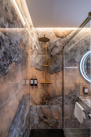 A modern bathroom with a marble wall, a gold showerhead, and a glass-enclosed mirror. - Sol Atelier | Apartments by Monaro* * * * * (Madrid)