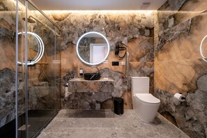 Een moderne badkamer met een glazen douchecabine, een marmeren wastafel, een toilet en een inbouwspiegel met verlichting.