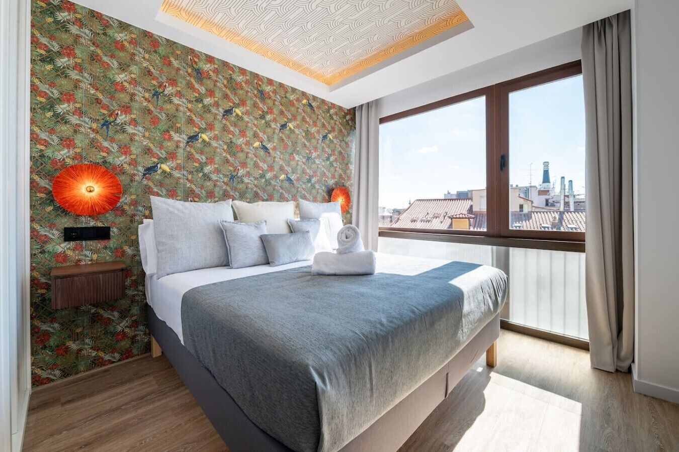 A modern hotel room with a large bed, a city view, and a patterned wallpaper.