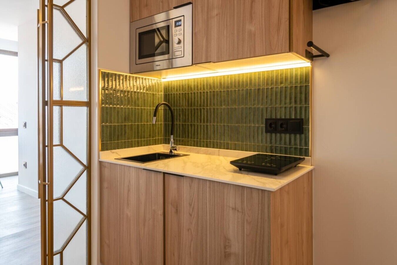 Une cuisine compacte dotée d’un four à micro-ondes encastré, d’un évier et d’un plan de travail.