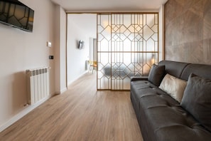 A modern living room with a sofa, a TV mounted on the wall, a radiator, and a decorative partition with geometric patterns. - Sol Atelier | Apartments by Monaro* * * * * (Madrid)
