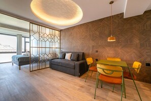 A modern living room with a sofa, a dining table with chairs, a decorative partition, and a patterned ceiling light. - Sol Atelier | Apartments by Monaro* * * * * (Madrid)