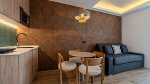 A modern kitchen with a wooden herringbone backsplash, a round dining table with chairs, and a black sofa in a living area. - Sol Atelier | Apartments by Monaro* * * * * (Madrid)