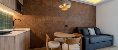 Una cocina moderna con un salpicadero de madera en patrón de espiga, una mesa redonda con sillas y un sofá negro en la sala de estar.