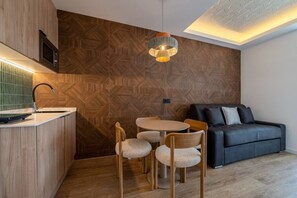 A modern kitchen with a wooden herringbone backsplash, a round dining table with chairs, and a black sofa in a living area. - Sol Atelier | Apartments by Monaro* * * * * (Madrid)