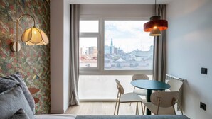 A hotel room with a bed, a table with chairs, a window with a view of the city, and a hanging lamp. - Sol Atelier | Apartments by Monaro* * * * * (Madrid)