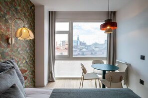 A hotel room with a bed, a table with chairs, a window with a view of the city, and a hanging lamp. - Sol Atelier | Apartments by Monaro* * * * * (Madrid)