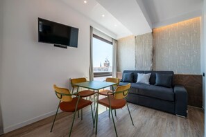 A modern living room with a sofa, a TV mounted on the wall, and a dining area with chairs and a table. - Sol Atelier | Apartments by Monaro* * * * * (Madrid)