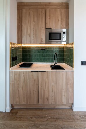 Une cuisine compacte avec des meubles en bois, un four à micro-ondes et un dosseret de carrelage vert.