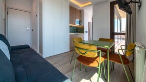 A compact living space with a sofa, dining table, chairs, a kitchen area, and a TV mounted on the wall. - Sol Atelier | Apartments by Monaro* * * * * (Madrid)
