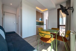 A compact living space with a sofa, dining table, chairs, a kitchen area, and a TV mounted on the wall. - Sol Atelier | Apartments by Monaro* * * * * (Madrid)