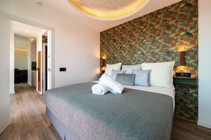 A modern hotel room with a large bed, a patterned wallpaper, and a hallway leading to another room. - Sol Atelier | Apartments by Monaro* * * * * (Madrid)