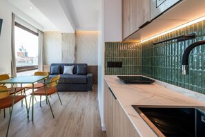 Une cuisine moderne dotée d’une cuisinière intégrée, un coin repas avec un canapé et des chaises, et une grande fenêtre offrant une vue sur la ville.
