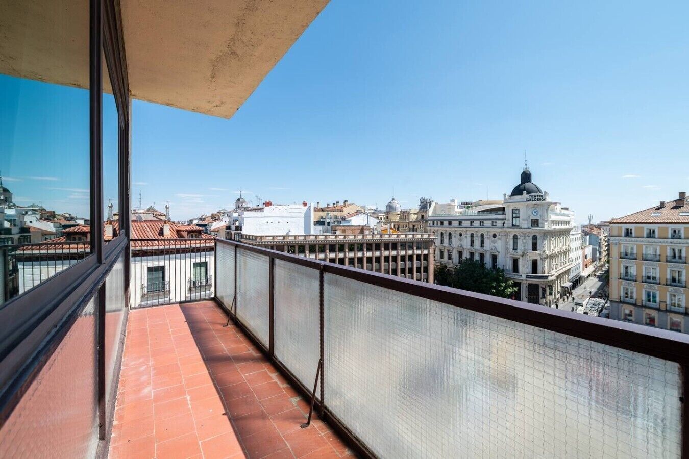 Un balcon offrant une vue sur les bâtiments de la ville, dont un théâtre.