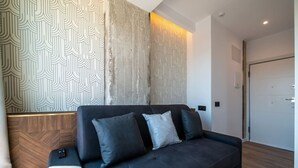A modern living room with a dark sofa, patterned wallpaper, and a wooden accent wall. - Sol Atelier | Apartments by Monaro* * * * * (Madrid)